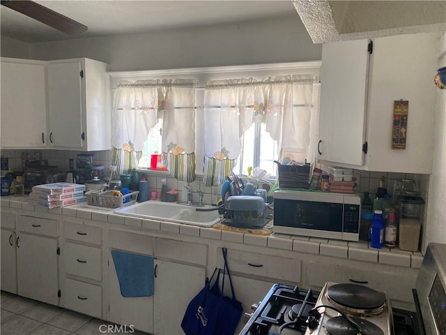 kitchen featuring decorative backsplash, white cabinets, light tile patterned floors, tile countertops, and sink