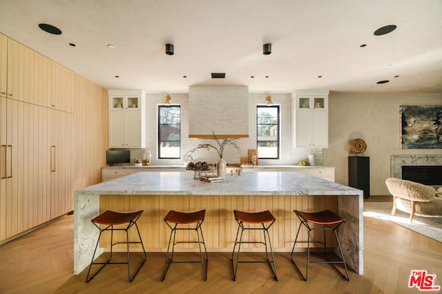 kitchen featuring white cabinetry, a breakfast bar area, decorative backsplash, light stone countertops, and a spacious island