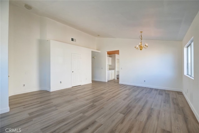 unfurnished room with lofted ceiling, a chandelier, and light hardwood / wood-style flooring