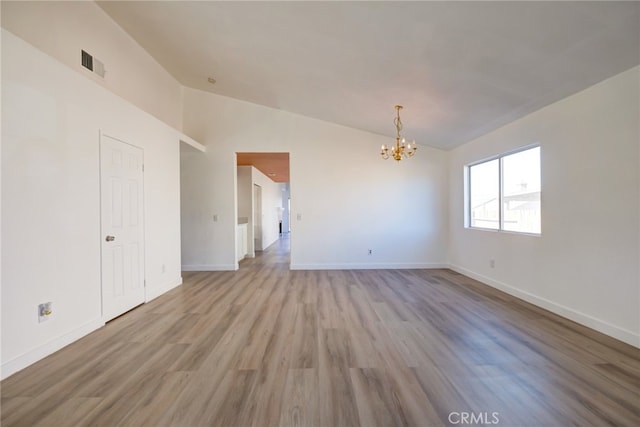 spare room featuring lofted ceiling, a notable chandelier, and light hardwood / wood-style floors