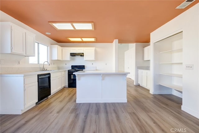 kitchen with light hardwood / wood-style flooring, white cabinets, black appliances, and a kitchen island