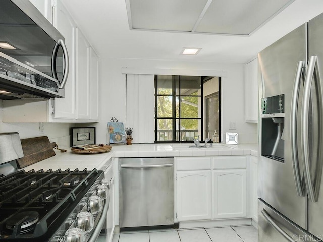 kitchen featuring light tile patterned flooring, tile counters, white cabinets, and stainless steel appliances