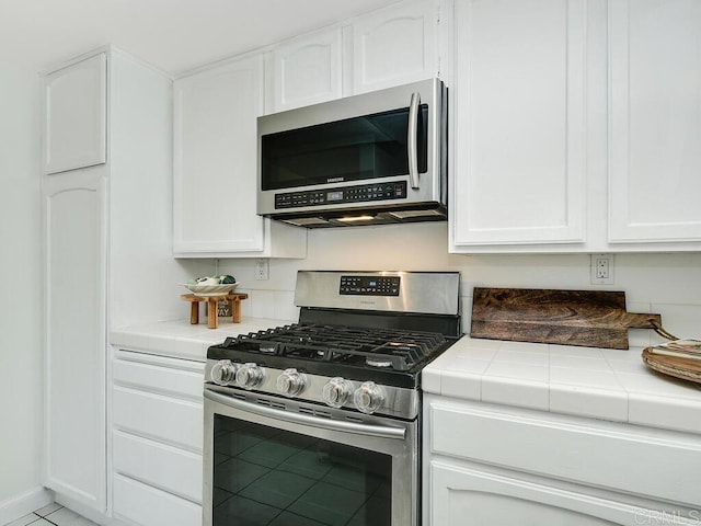 kitchen with appliances with stainless steel finishes, tile counters, white cabinets, and light tile patterned floors