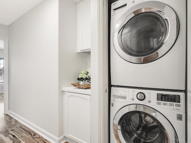 laundry area with stacked washer / drying machine and light hardwood / wood-style flooring