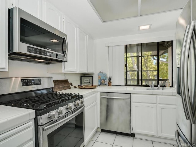 kitchen with white cabinetry, tile countertops, appliances with stainless steel finishes, and light tile patterned floors