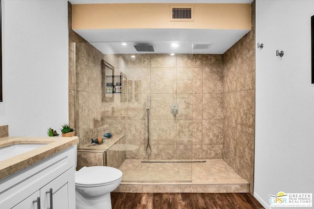 bathroom featuring a tile shower, toilet, vanity, and hardwood / wood-style flooring