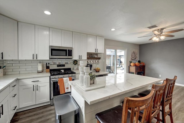 kitchen with stainless steel appliances, white cabinetry, a kitchen island, and light stone counters