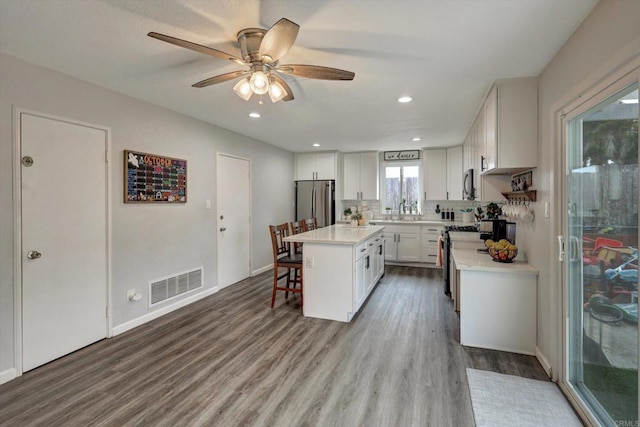 kitchen with hardwood / wood-style flooring, a breakfast bar area, appliances with stainless steel finishes, white cabinetry, and a center island