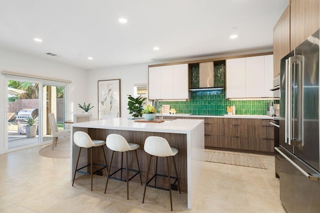 kitchen featuring a center island, high end fridge, wall chimney range hood, and white cabinetry