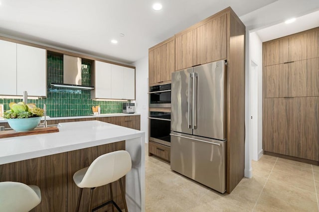 kitchen with appliances with stainless steel finishes, tasteful backsplash, white cabinetry, and wall chimney range hood