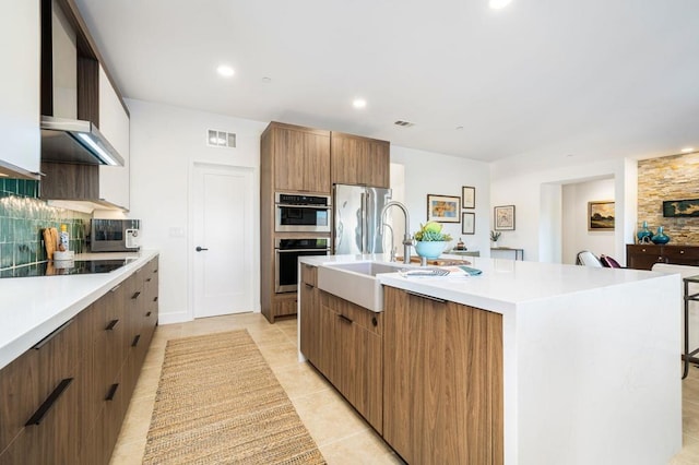 kitchen featuring decorative backsplash, appliances with stainless steel finishes, a kitchen island with sink, sink, and light tile patterned flooring