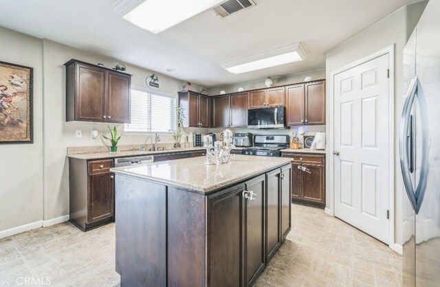 kitchen with light stone counters, stainless steel appliances, dark brown cabinetry, and a center island