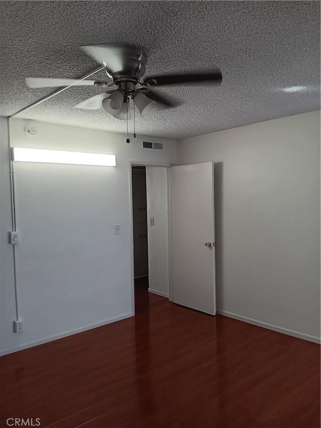 empty room with a textured ceiling, ceiling fan, and dark hardwood / wood-style floors