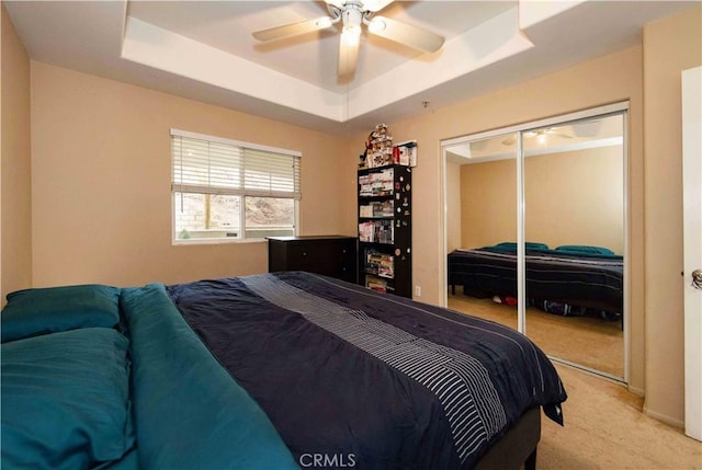 carpeted bedroom featuring a tray ceiling, a closet, and ceiling fan