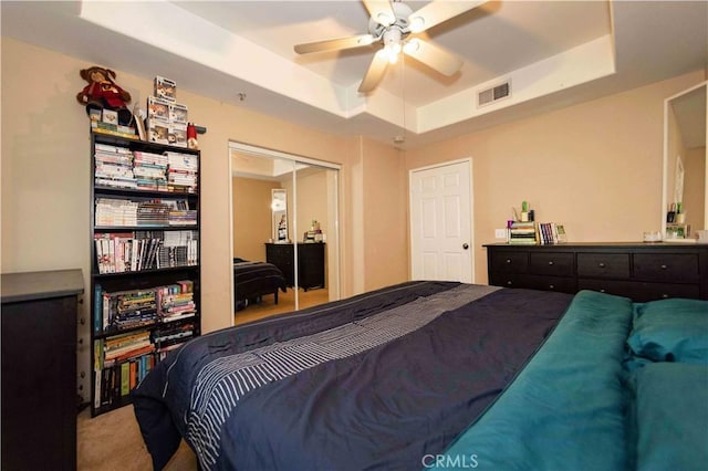 carpeted bedroom with a raised ceiling, ceiling fan, and a closet