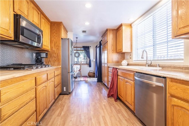 kitchen featuring appliances with stainless steel finishes, backsplash, sink, light hardwood / wood-style flooring, and hanging light fixtures