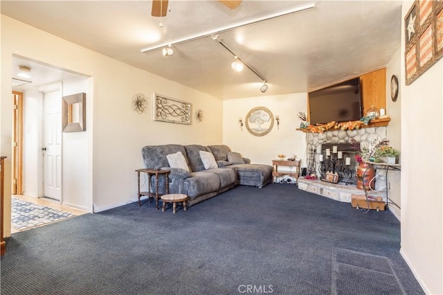 carpeted living room with a stone fireplace, ceiling fan, and track lighting