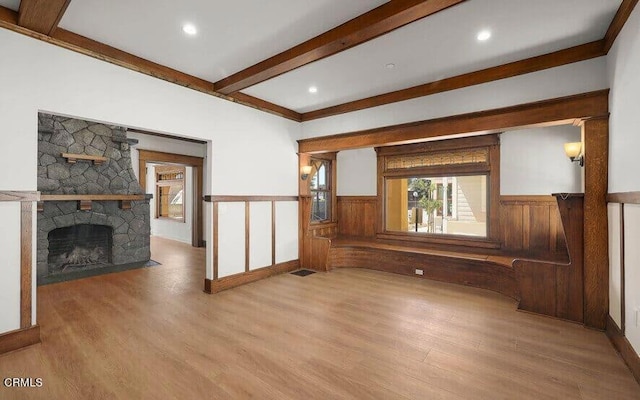 unfurnished living room featuring beam ceiling, light hardwood / wood-style floors, a stone fireplace, and crown molding