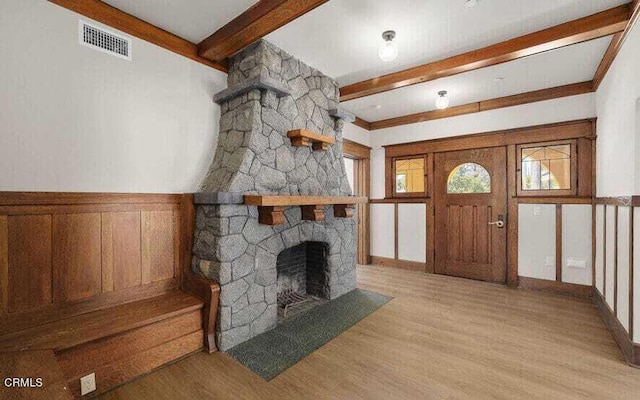 living room with beamed ceiling, light hardwood / wood-style floors, and a stone fireplace