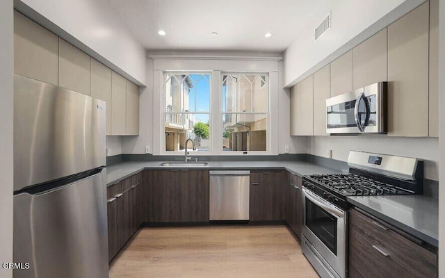 kitchen with appliances with stainless steel finishes, light hardwood / wood-style floors, dark brown cabinets, and sink