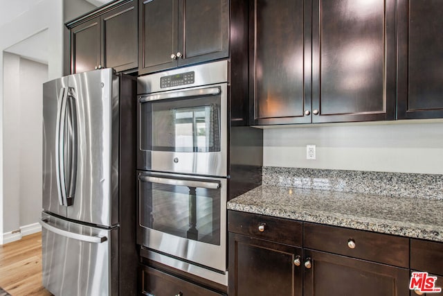 kitchen with dark brown cabinetry, light stone countertops, appliances with stainless steel finishes, and light hardwood / wood-style flooring