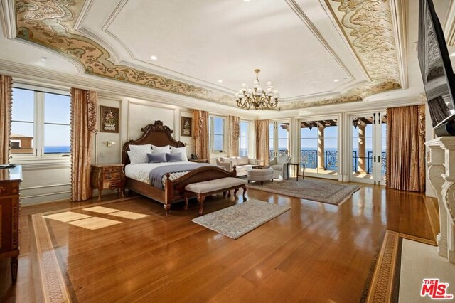 bedroom featuring a tray ceiling, wood-type flooring, ornamental molding, and an inviting chandelier