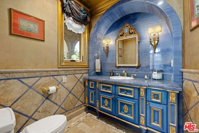 bathroom with toilet, ornamental molding, vanity, and tile walls