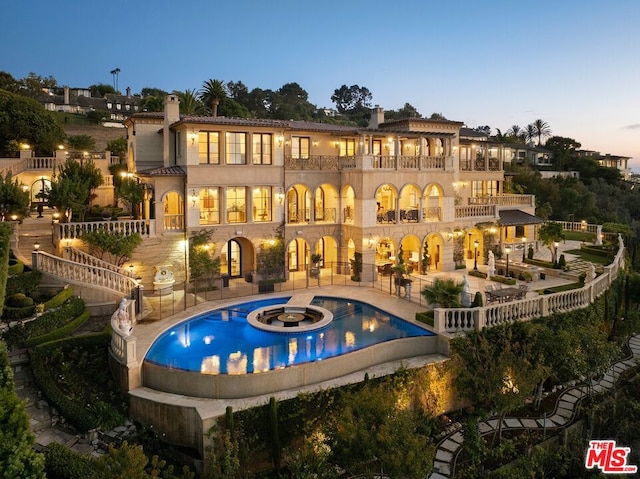 back house at dusk with a patio, a pool with hot tub, and a balcony