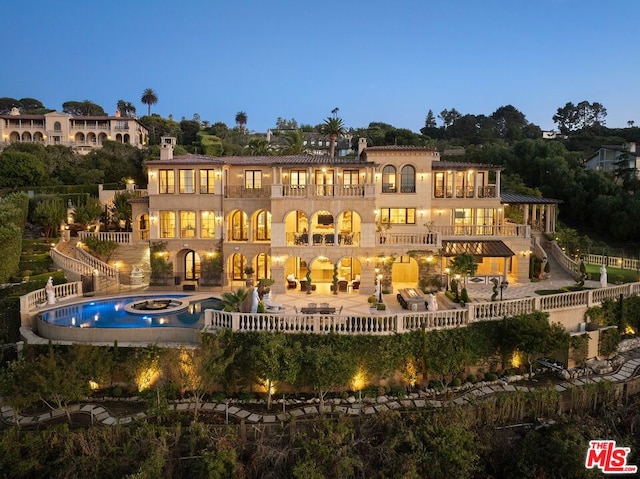 back house at dusk with a patio area, an in ground hot tub, and a balcony