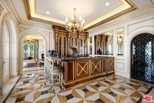 bar featuring hanging light fixtures, light tile patterned floors, an inviting chandelier, a tray ceiling, and ornamental molding