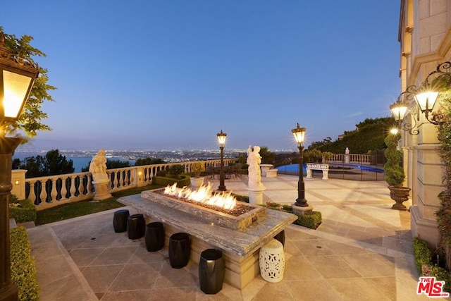 patio terrace at dusk featuring an outdoor fire pit and a pool