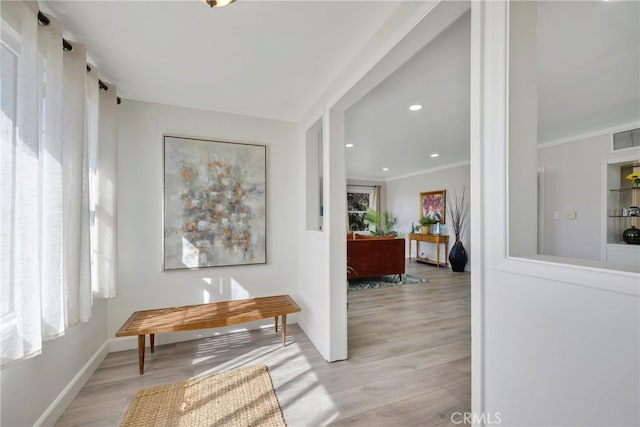 hall with a wealth of natural light, crown molding, and light wood-type flooring