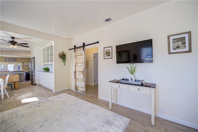 unfurnished living room with ceiling fan, a barn door, and light hardwood / wood-style floors