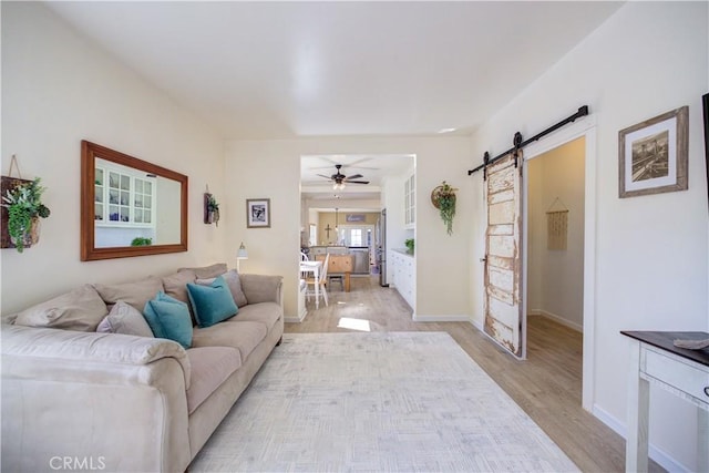 living room with ceiling fan, a barn door, and light hardwood / wood-style floors