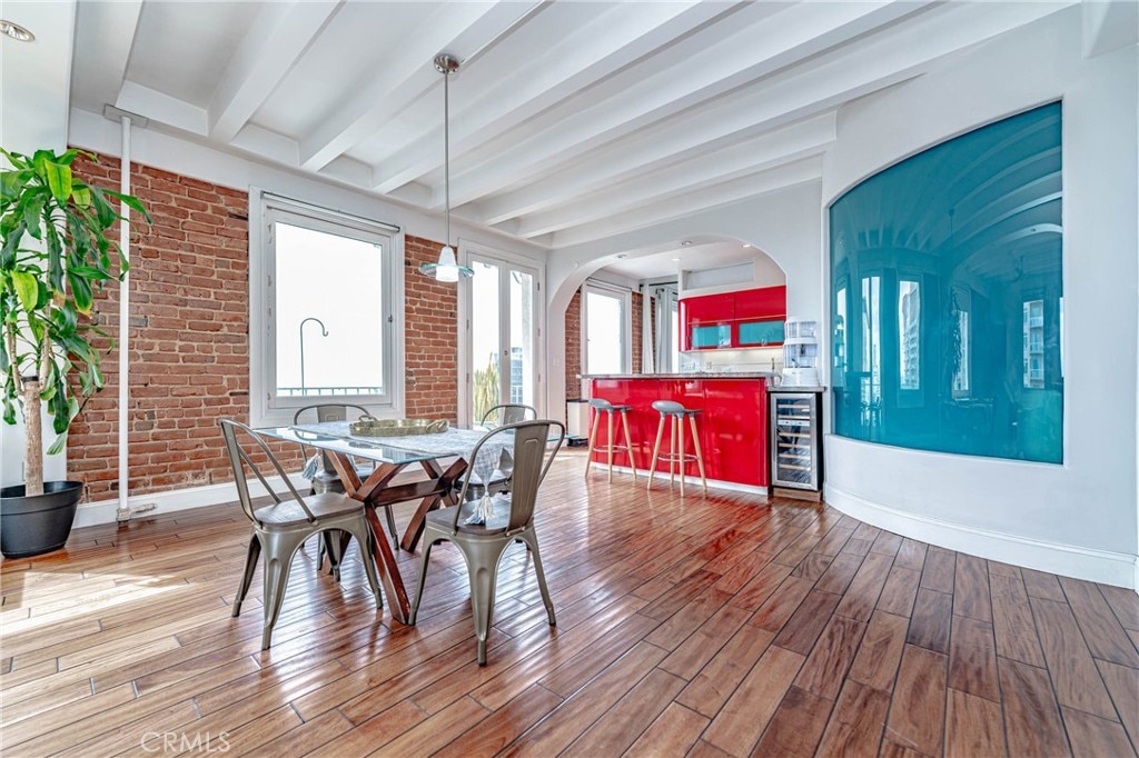 dining area featuring beverage cooler, beamed ceiling, brick wall, and hardwood / wood-style floors