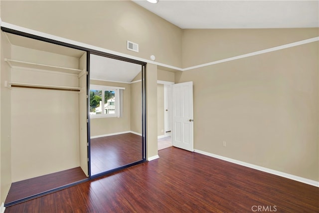 unfurnished bedroom featuring lofted ceiling, a closet, visible vents, hardwood / wood-style floors, and baseboards