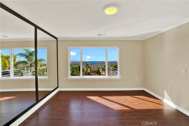 empty room with visible vents, crown molding, and wood finished floors