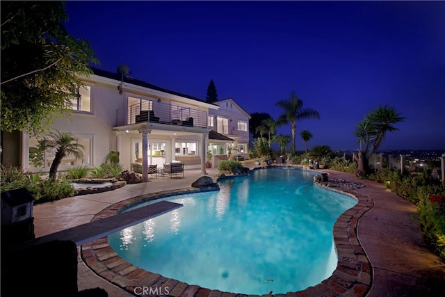 pool at twilight with an outdoor pool, a patio, and a diving board