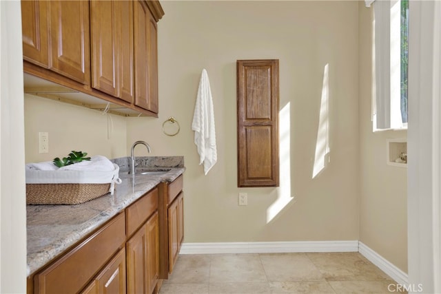 kitchen featuring light stone counters, brown cabinets, light tile patterned floors, a sink, and baseboards