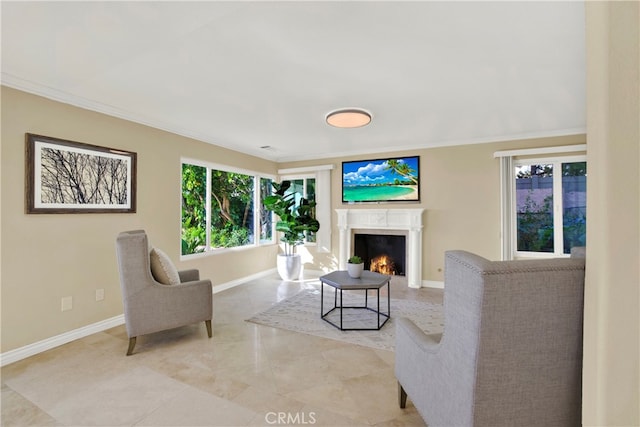 living area featuring crown molding, a lit fireplace, and baseboards