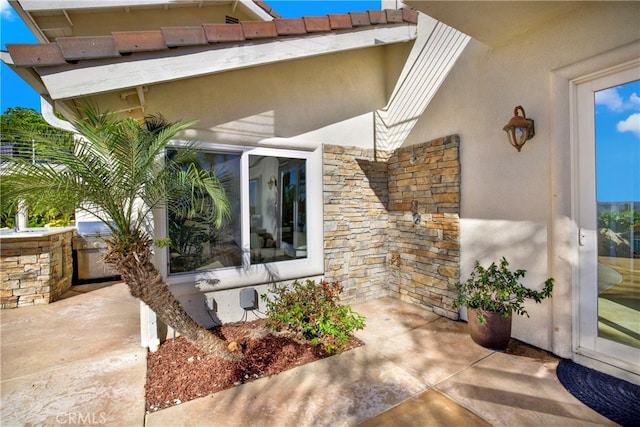 view of exterior entry featuring stone siding, an outdoor kitchen, and stucco siding