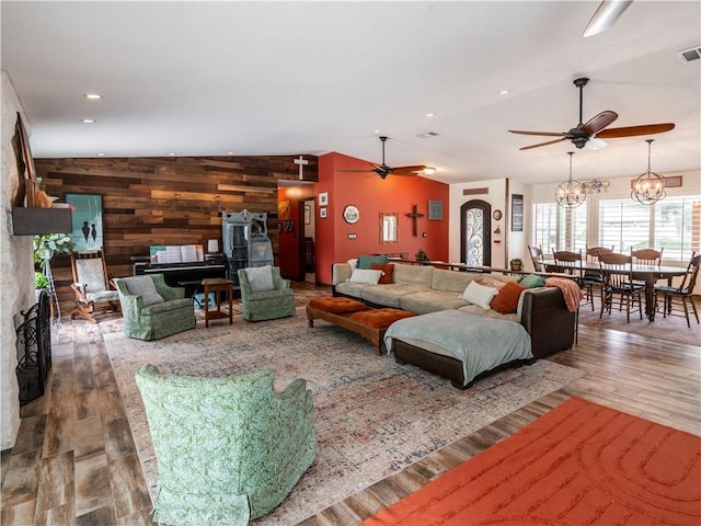 living room with ceiling fan with notable chandelier, hardwood / wood-style floors, wooden walls, and lofted ceiling