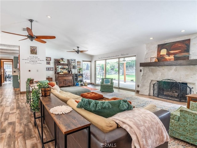 living room featuring hardwood / wood-style floors, ceiling fan, and a stone fireplace