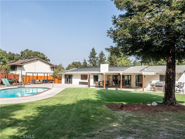 rear view of property featuring a fenced in pool, a patio area, a lawn, and solar panels