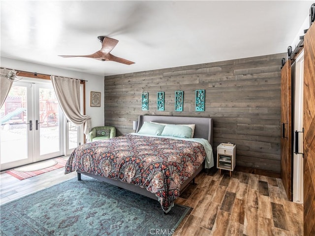 bedroom featuring access to outside, wooden walls, ceiling fan, and wood-type flooring