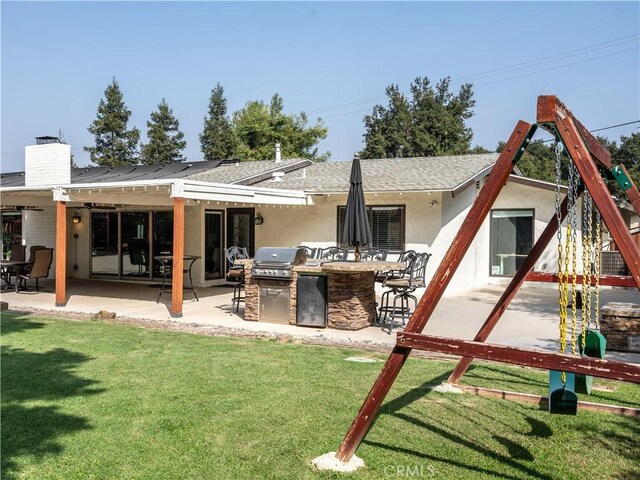 back of house featuring a lawn, an outdoor kitchen, and a patio area