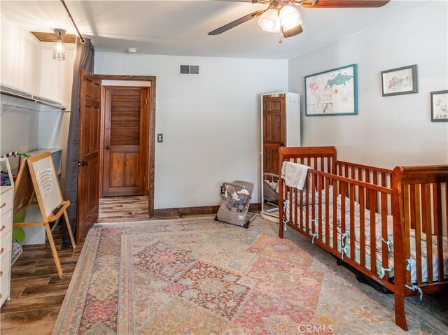 bedroom featuring ceiling fan, hardwood / wood-style floors, and a crib