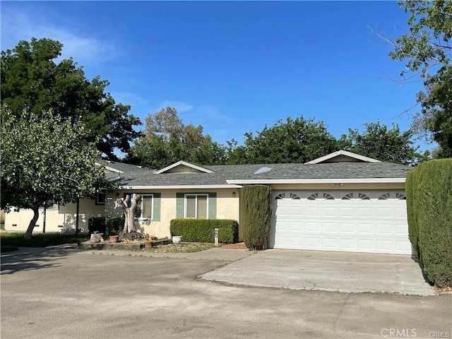 single story home with a garage, concrete driveway, a shingled roof, and stucco siding