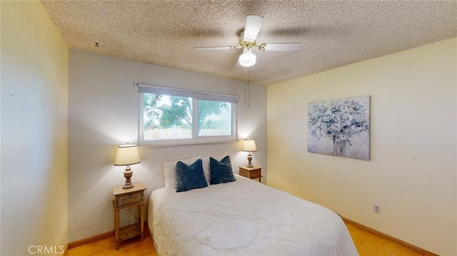 bedroom featuring light wood finished floors, a ceiling fan, baseboards, and a textured ceiling