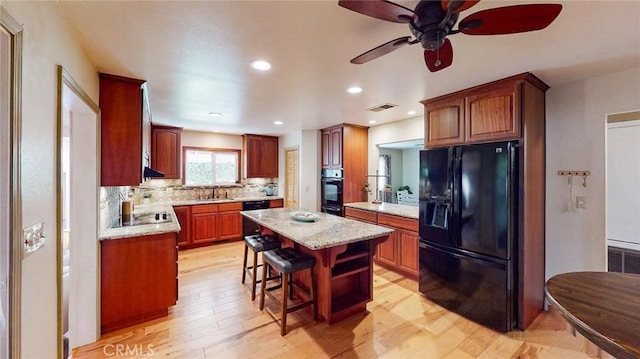 kitchen featuring a breakfast bar, a sink, a kitchen island, visible vents, and black appliances